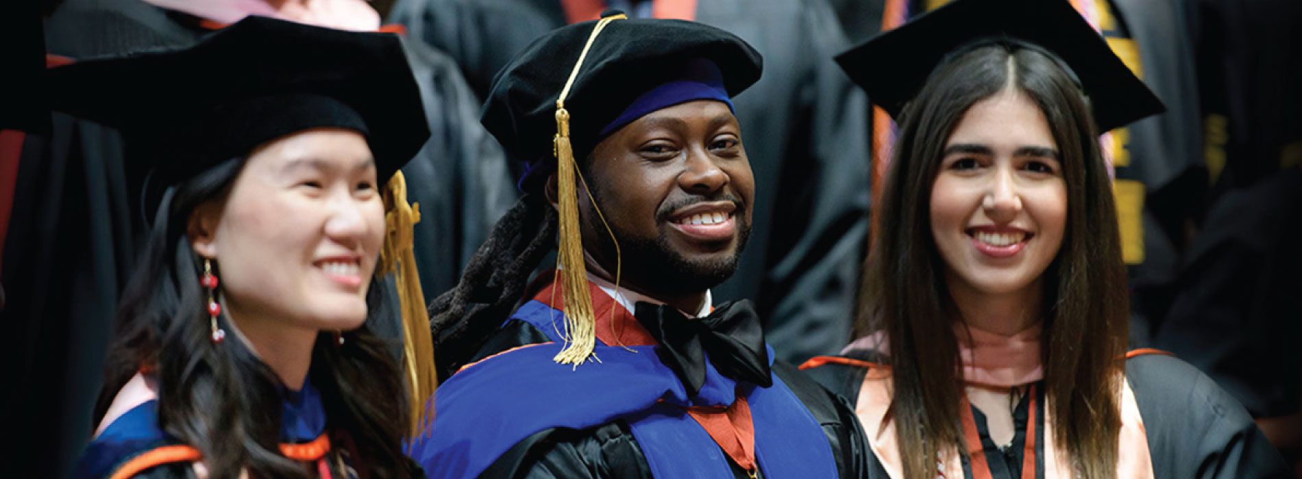 group of three graduates smiling in cap and gown