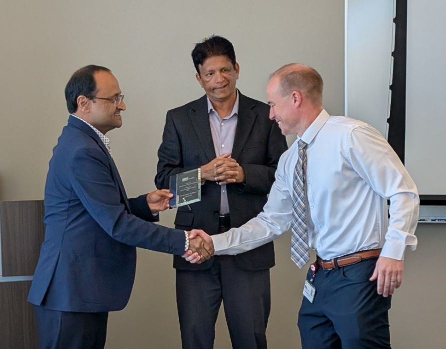 Dr. Vineet Gupta presents a plaque to Dr. Chris Zahner, shaking his hand. Dr. Sundeep Mattamana is pictured behind them.