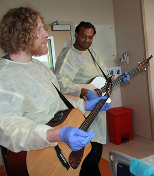 Two men wearing PPE are playing guitar and singing