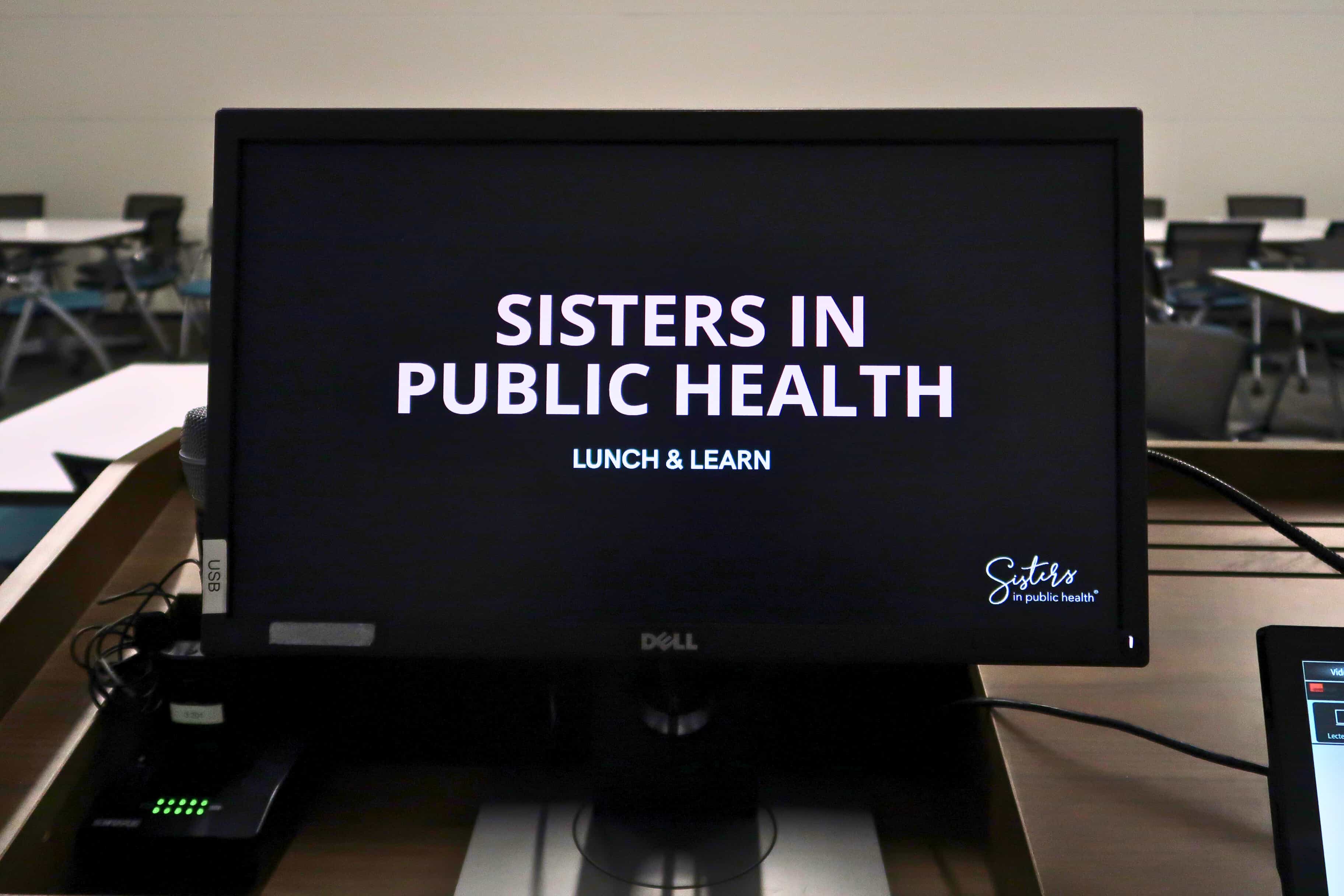 A photo from the podium depicting the title page "Sisters in Public Health: Lunch & Learn".